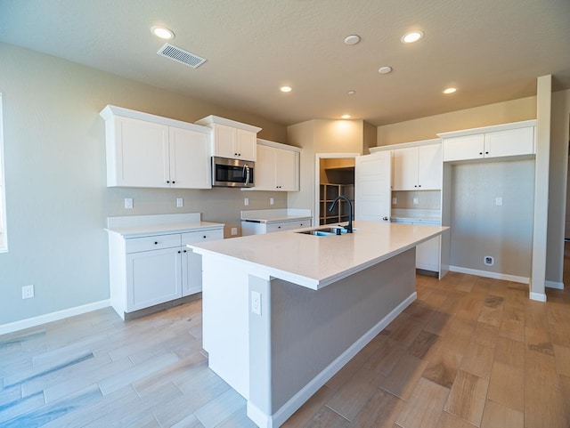 917 Beaver Pond Loop, Madera, CA 93636 - kitchen with stainless steel microwave, a sink, an island with sink, light wood-style flooring, and white cabinetry