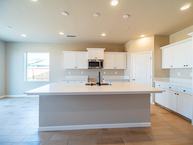 917 Beaver Pond Loop, Madera, CA 93636 - kitchen with stainless steel microwave, a sink, a center island with sink, recessed lighting, and white cabinets
