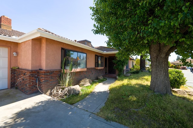 view of front of property with a chimney, brick siding, stucco siding, and a tile roof