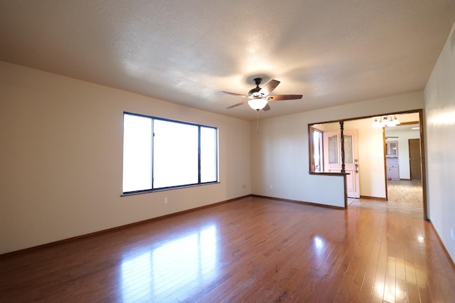 spare room with wood finished floors, baseboards, ceiling fan, a textured ceiling, and a chandelier