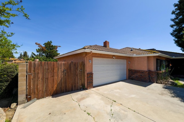 view of front of house featuring a chimney, brick siding, a gate, an attached garage, and driveway