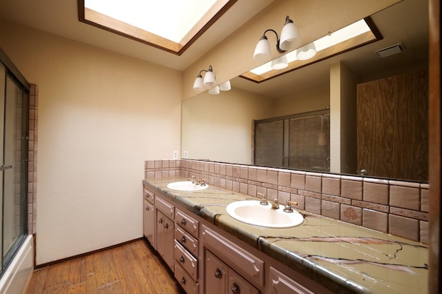 bathroom featuring wood-type flooring, baseboards, decorative backsplash, double vanity, and enclosed tub / shower combo