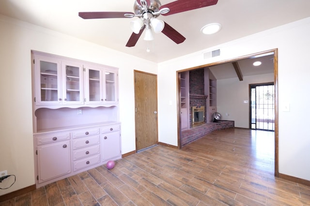 unfurnished living room featuring a ceiling fan, baseboards, a brick fireplace, and wood finished floors
