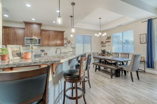 716 Mesa Dr S, Madera, CA 93636 - kitchen with stainless steel microwave, tasteful backsplash, a breakfast bar area, a raised ceiling, and light wood-style floors
