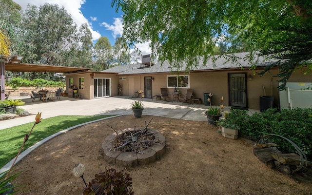 rear view of property featuring stucco siding, a fire pit, and a patio