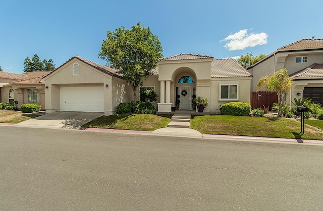 1073 E Pennsylvania Ave, Fresno, CA 93720 - mediterranean / spanish house with an attached garage, stucco siding, a tile roof, concrete driveway, and a front lawn