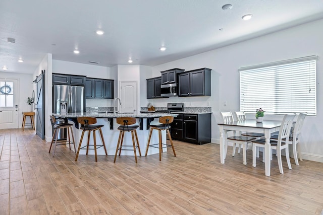 6772 E Ramona Way, Fresno, CA 93727 - kitchen featuring stainless steel appliances, a kitchen bar, light stone counters, light wood-style floors, and a kitchen island with sink