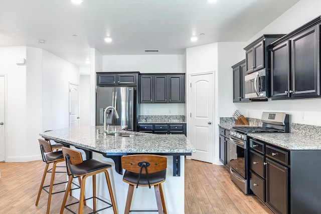 6772 E Ramona Way, Fresno, CA 93727 - kitchen featuring stainless steel appliances, light wood-style floors, a breakfast bar area, light stone counters, and a kitchen island with sink