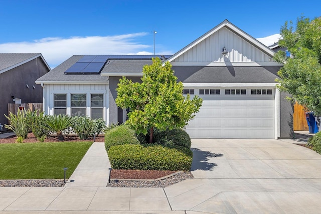 6772 E Ramona Way, Fresno, CA 93727 - view of front facade with roof mounted solar panels, driveway, an attached garage, board and batten siding, and a front lawn
