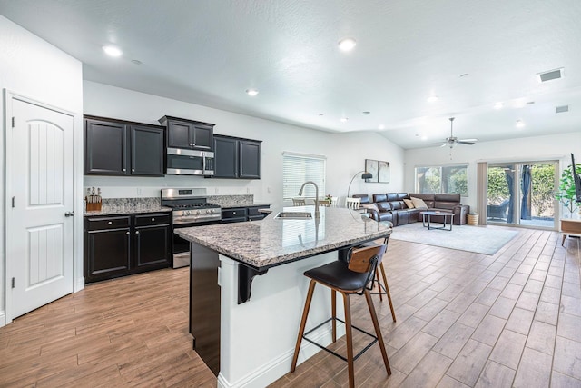 6772 E Ramona Way, Fresno, CA 93727 - kitchen featuring stainless steel appliances, a sink, light wood-style flooring, open floor plan, and a kitchen bar
