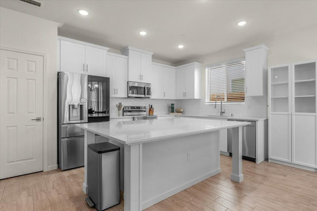 kitchen featuring stainless steel appliances, a center island, white cabinets, tasteful backsplash, and light countertops
