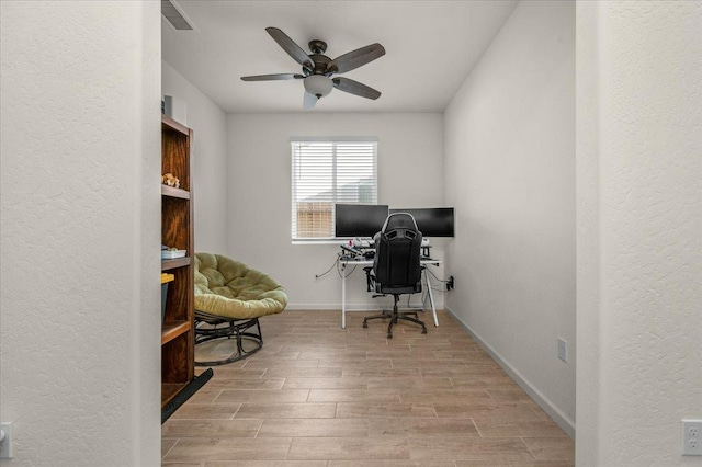 home office with wood finished floors, a ceiling fan, a textured wall, and baseboards