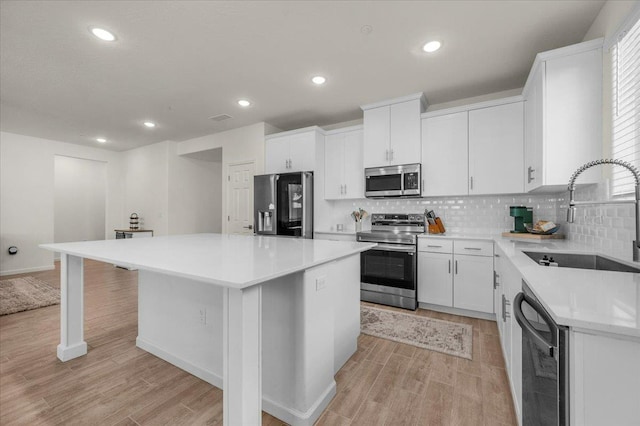 kitchen with appliances with stainless steel finishes, a sink, light wood-type flooring, a center island, and recessed lighting