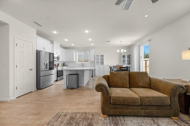 living room with a chandelier, light wood-style flooring, recessed lighting, ceiling fan, and baseboards