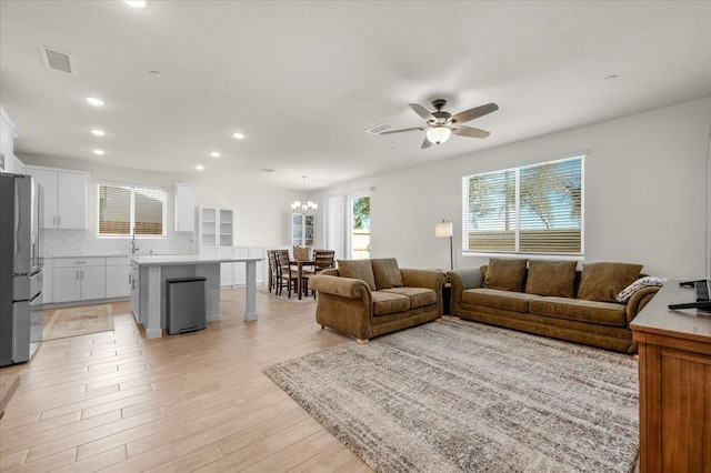 living room featuring a ceiling fan, light wood-style floors, a chandelier, and recessed lighting