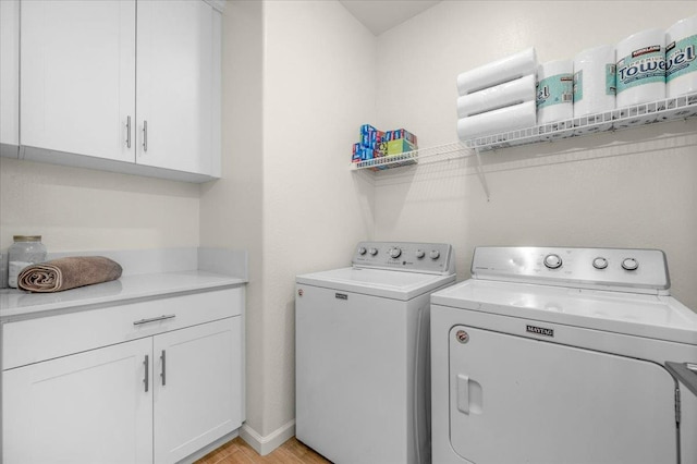 clothes washing area with washing machine and dryer, cabinet space, and light wood-style floors