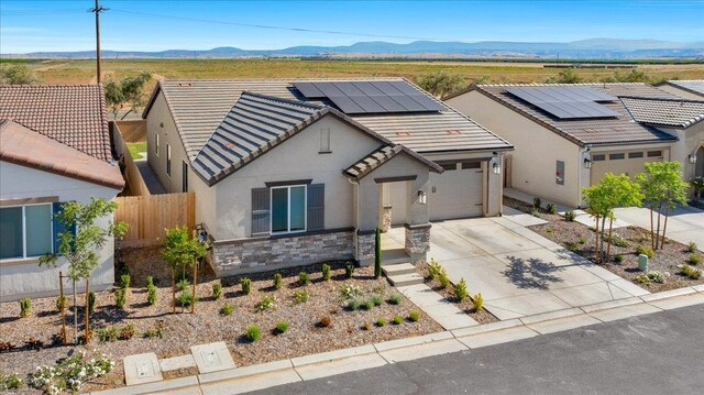 view of front facade with driveway, stucco siding, stone siding, roof mounted solar panels, and an attached garage