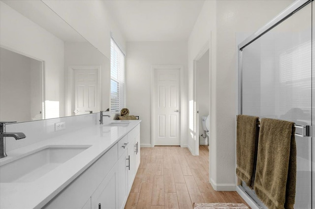 bathroom featuring wood finished floors, a shower stall, baseboards, and double vanity