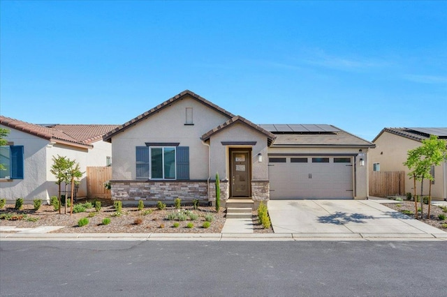 view of front of property with an attached garage, roof mounted solar panels, driveway, fence, and stone siding