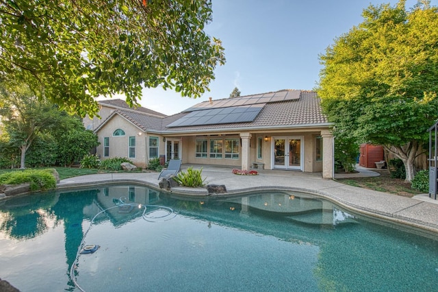 rear view of house with french doors, a tiled roof, roof mounted solar panels, a patio area, and stucco siding