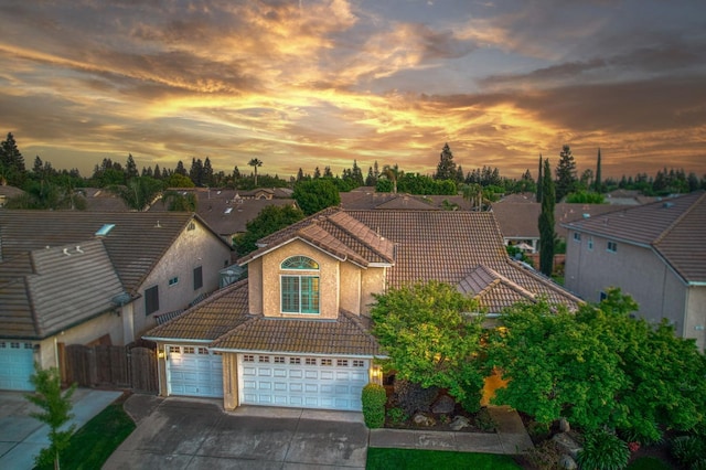view of front facade with a tiled roof, concrete driveway, fence, stucco siding, and a residential view