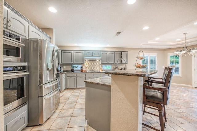 kitchen featuring appliances with stainless steel finishes, gray cabinets, recessed lighting, a breakfast bar area, and backsplash