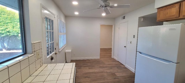 kitchen featuring freestanding refrigerator, tile countertops, ceiling fan, brown cabinetry, and wood finished floors