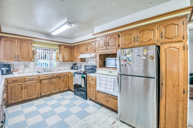 kitchen with stainless steel appliances, under cabinet range hood, brown cabinets, and backsplash