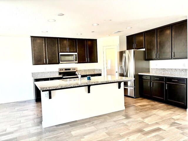 2158 W Ambassador Way, Hanford, CA 93230 - kitchen featuring stainless steel appliances, a kitchen breakfast bar, light stone countertops, an island with sink, and dark brown cabinets