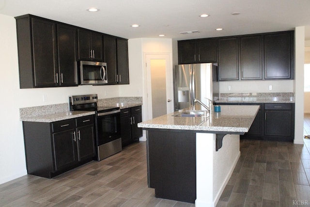 2158 W Ambassador Way, Hanford, CA 93230 - kitchen with appliances with stainless steel finishes, a sink, wood finished floors, a kitchen island with sink, and light stone counters