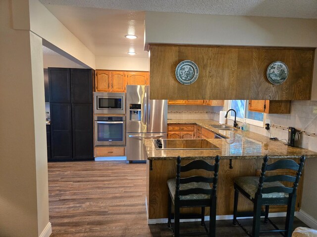 1489 Celeste Ave, Clovis, CA 93611 - kitchen with appliances with stainless steel finishes, a sink, a peninsula, wood finished floors, and stone counters