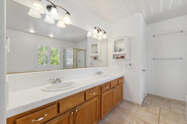 full bath featuring a shower stall, a chandelier, double vanity, stone tile flooring, and baseboards