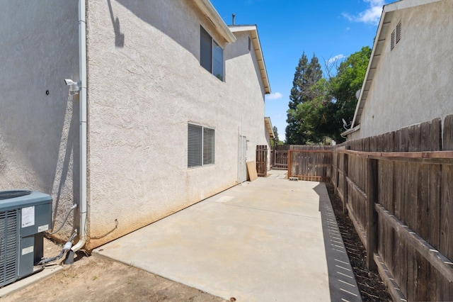 view of side of property with stucco siding, a fenced backyard, central AC, and a patio area
