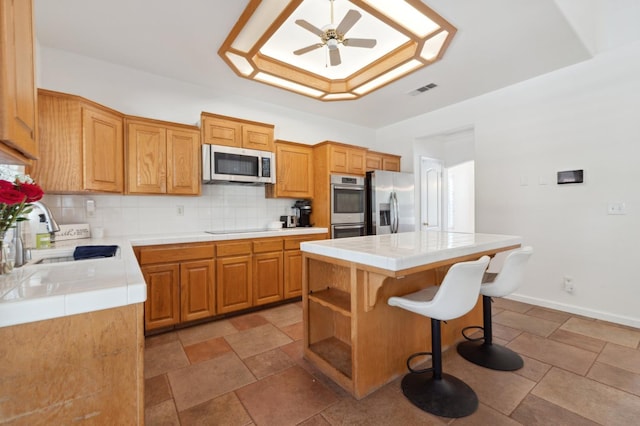 kitchen with stainless steel appliances, tile countertops, a sink, and backsplash