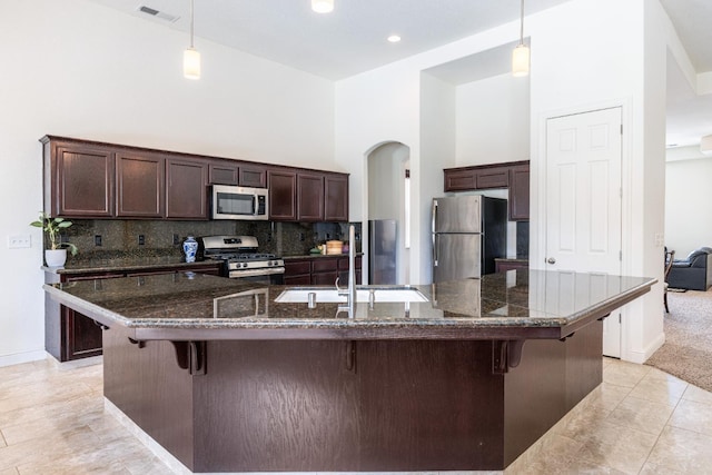 5279 N Ensanada Ave, Fresno, CA 93723 - kitchen featuring appliances with stainless steel finishes, dark brown cabinetry, arched walkways, a breakfast bar area, and a high ceiling