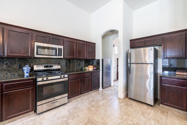 5279 N Ensanada Ave, Fresno, CA 93723 - kitchen featuring appliances with stainless steel finishes, arched walkways, dark stone countertops, dark brown cabinets, and a towering ceiling