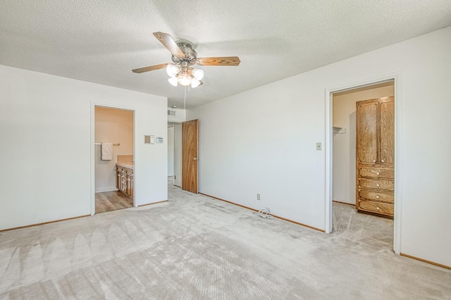 unfurnished bedroom featuring a spacious closet, carpet, baseboards, ensuite bath, and a textured ceiling