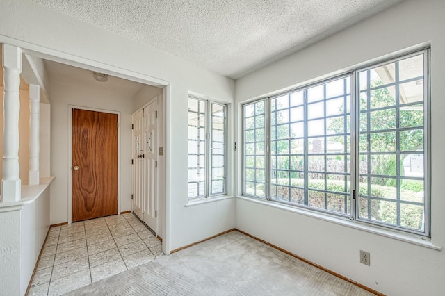 foyer entrance with a textured ceiling, baseboards, and light carpet