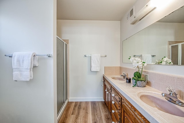 full bath featuring a stall shower, wood finished floors, baseboards, double vanity, and backsplash
