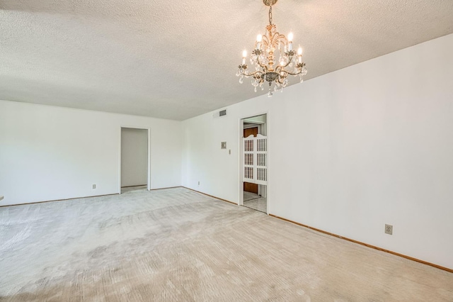 spare room with a chandelier, a textured ceiling, baseboards, and light carpet