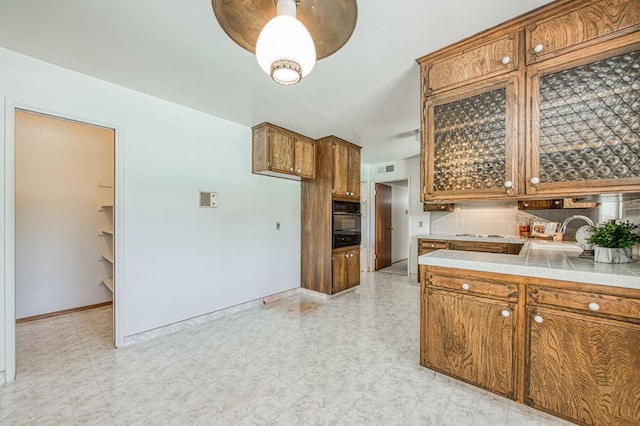 kitchen featuring oven, brown cabinets, a sink, decorative backsplash, and light flooring