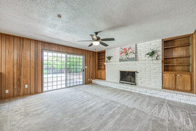 unfurnished living room featuring wood walls, a fireplace, a ceiling fan, built in features, and a textured ceiling