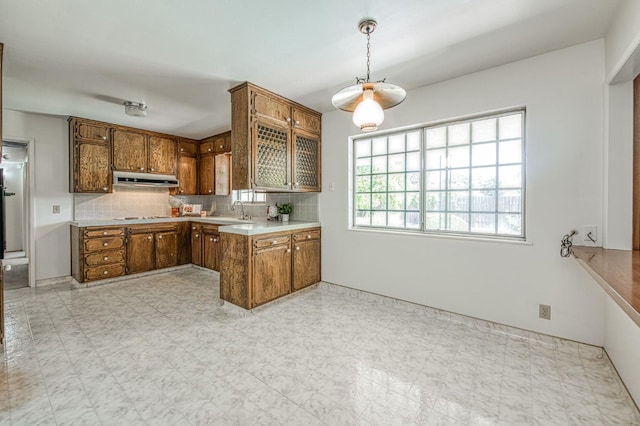 kitchen featuring brown cabinets, under cabinet range hood, backsplash, cooktop, and light countertops
