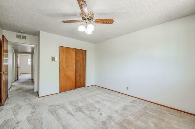 unfurnished bedroom featuring a closet, light colored carpet, baseboards, a textured ceiling, and a ceiling fan