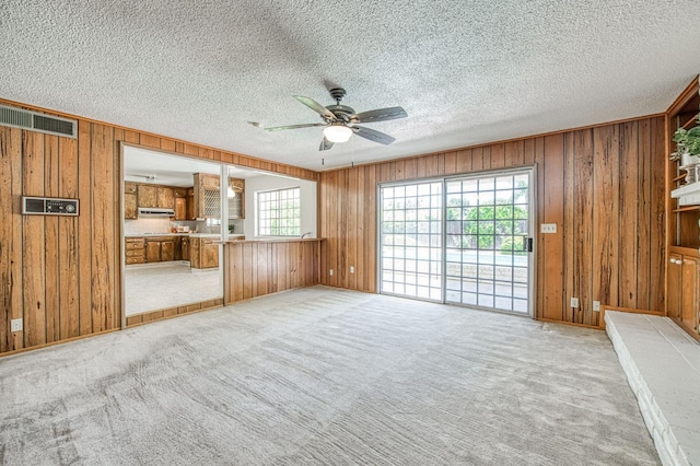 unfurnished living room with wooden walls, ceiling fan, a textured ceiling, and light colored carpet