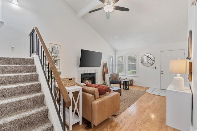 living area with a ceiling fan, high vaulted ceiling, light wood-style flooring, a fireplace, and beamed ceiling