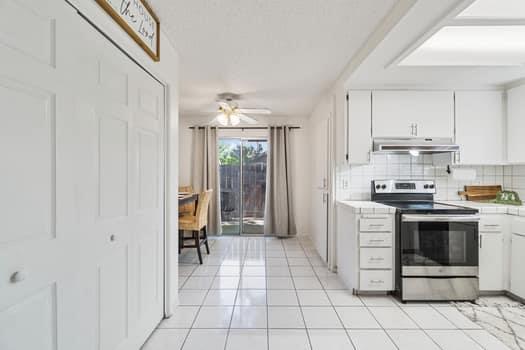 kitchen with stainless steel range with electric cooktop, under cabinet range hood, tasteful backsplash, white cabinetry, and ceiling fan