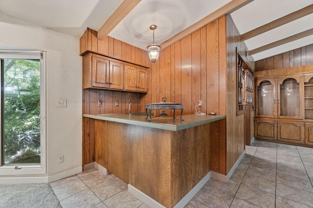 kitchen with brown cabinetry, wooden walls, light tile patterned floors, light countertops, and beam ceiling