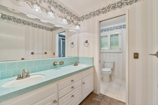 full bathroom with toilet, double vanity, tile patterned flooring, baseboards, and wallpapered walls