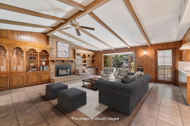 living room featuring wooden walls, light tile patterned flooring, a large fireplace, and ceiling fan